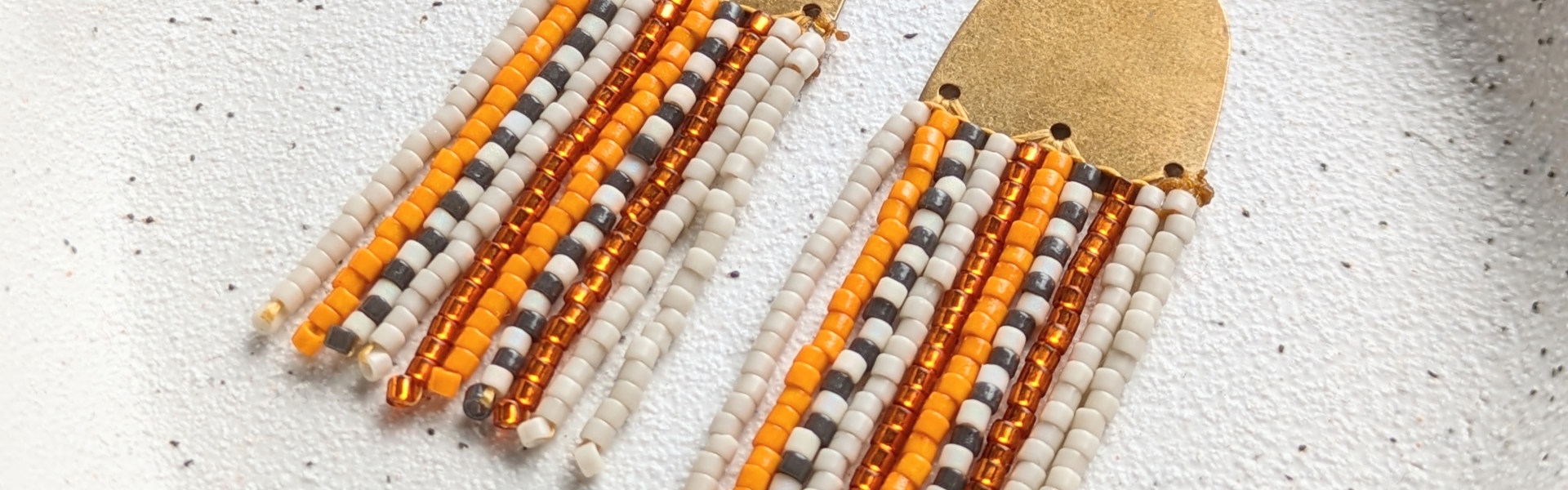 Main image: beaded fringe earrings, in cream, yellow gold, white and black seed beads with  gold metal connector frame. 