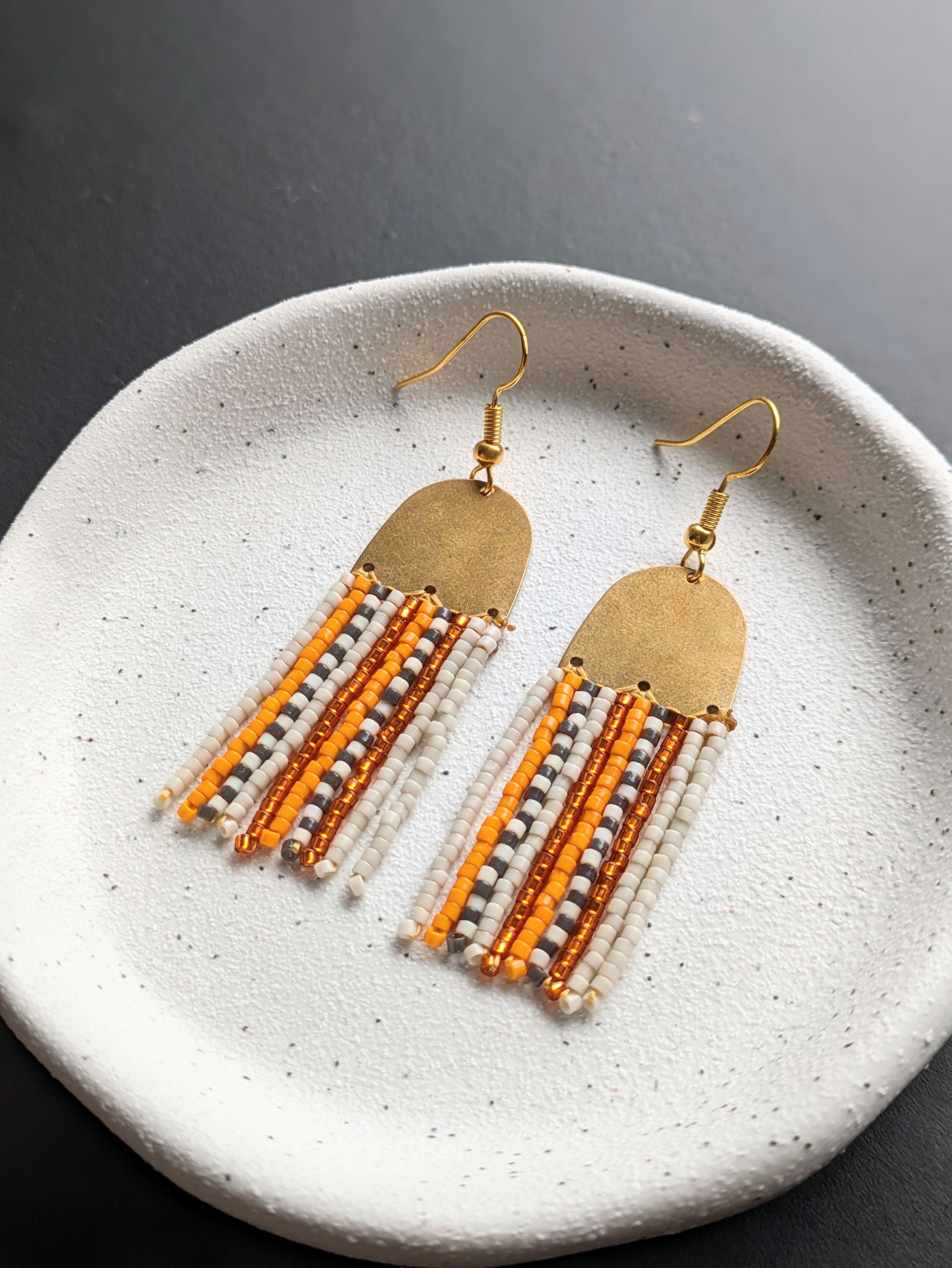 Main image: beaded fringe earrings, in cream, yellow gold, white and black seed beads with  gold metal connector frame. 