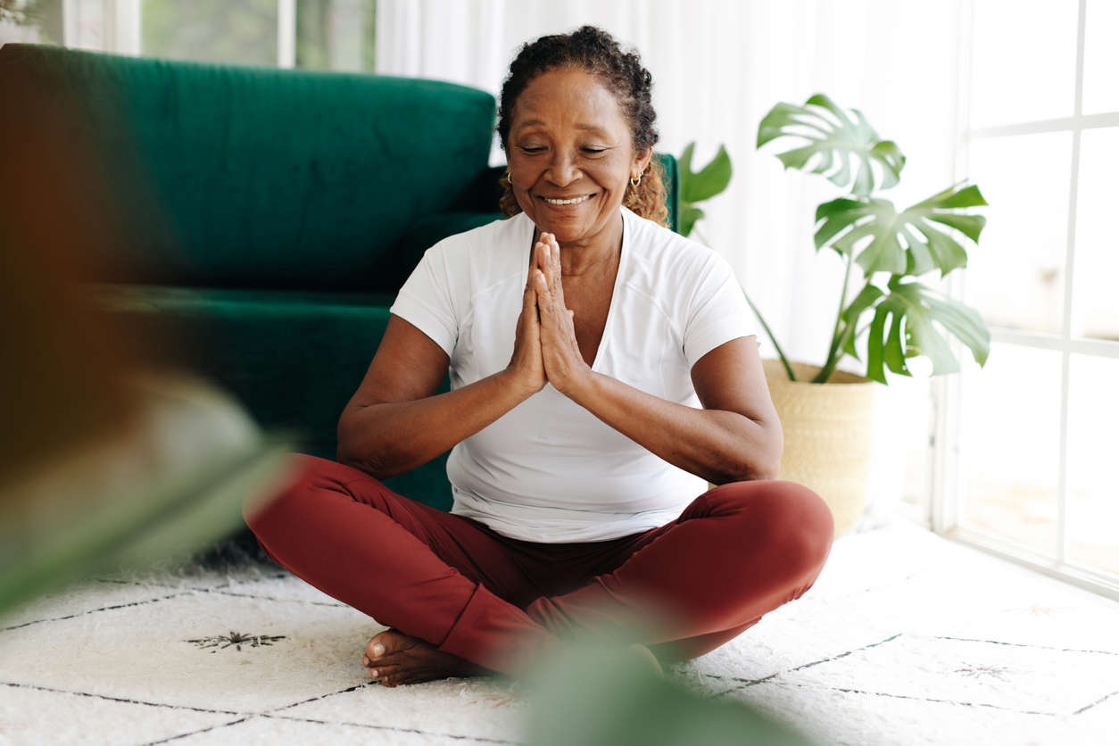 a woman sat cross legged with eyes closed in the living room doing yoga practice at home