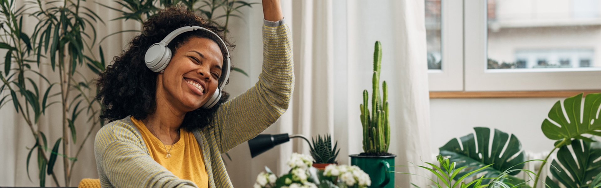 a woman sat down on the sofa at home wearing headphones dancing along to an online dance class