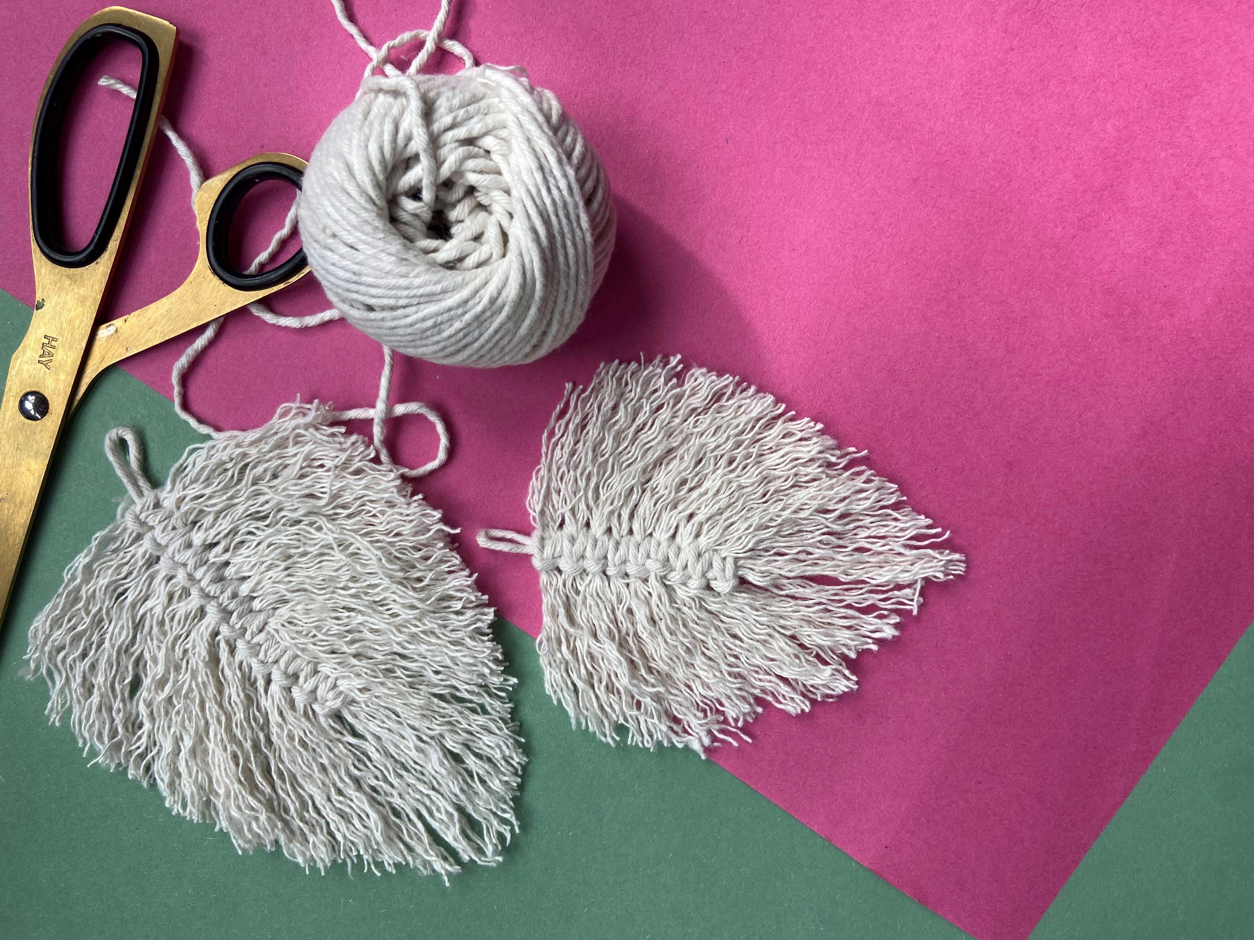 two macrame leaves resting on colourful paper with yellow scissors