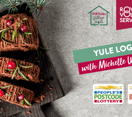 a chocolate Christmas yule log on a wooden board decorated with red cranberries and green festive herbs
