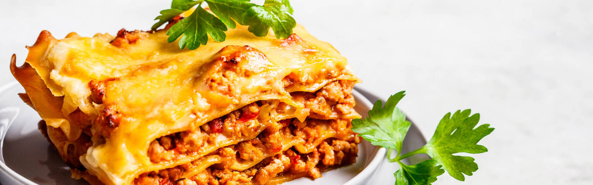 a slice of lasagne topped with green herbs on a white plate