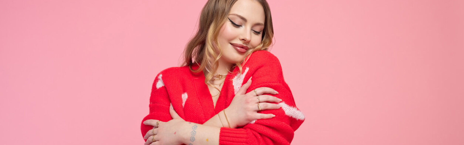 Valentine's portrait of a lovely young woman in a red heart cardigan, demonstrating self-love, set against a vibrant pink backdrop.