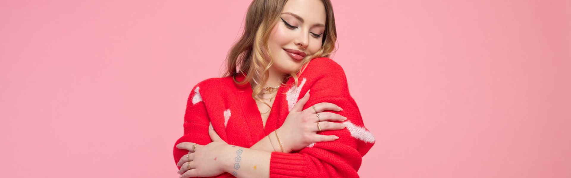 Valentine's portrait of a lovely young woman in a red heart cardigan, demonstrating self-love, set against a vibrant pink backdrop.