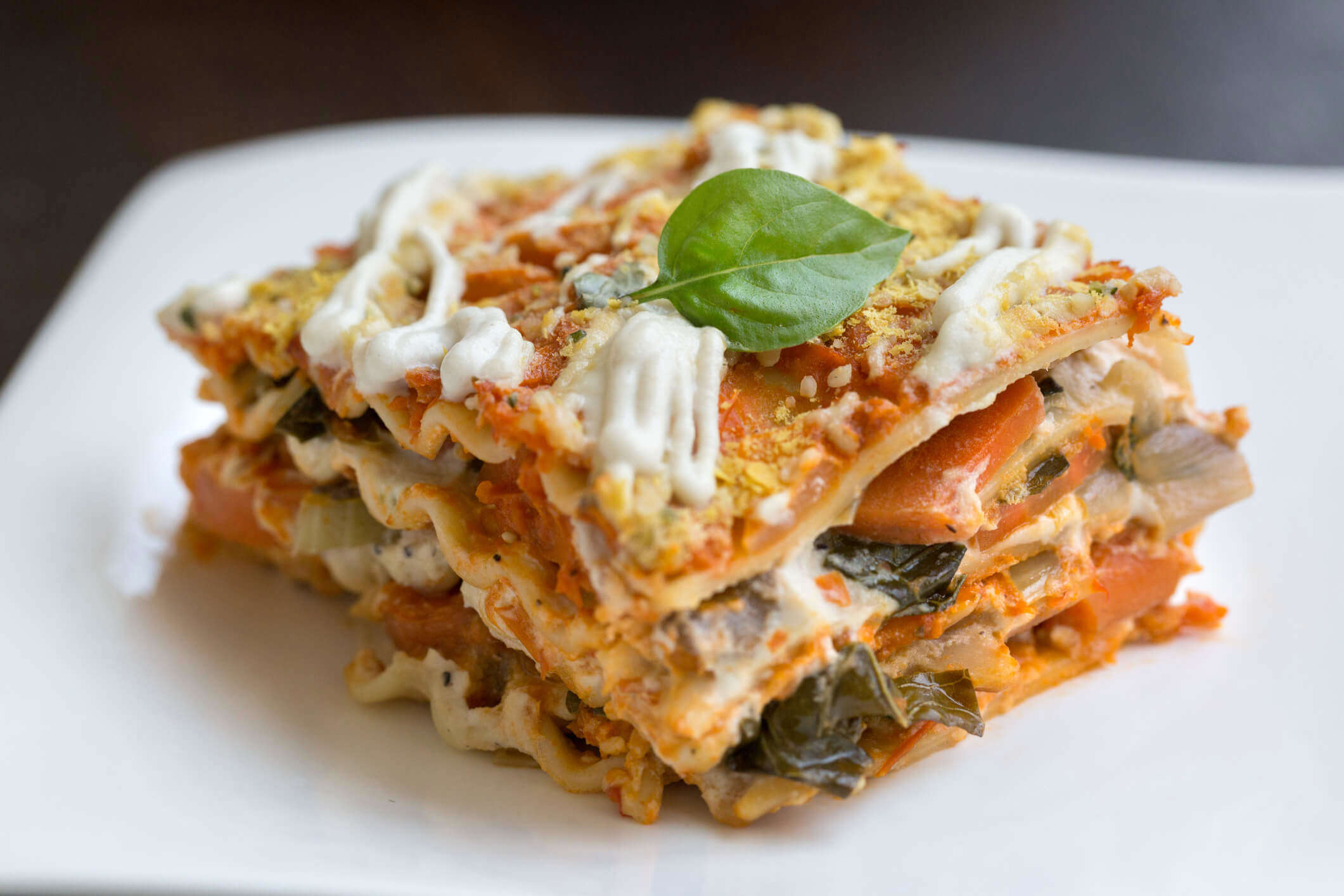 a slice of lentil ricotta spinach lasagne topped with a basil leaf
