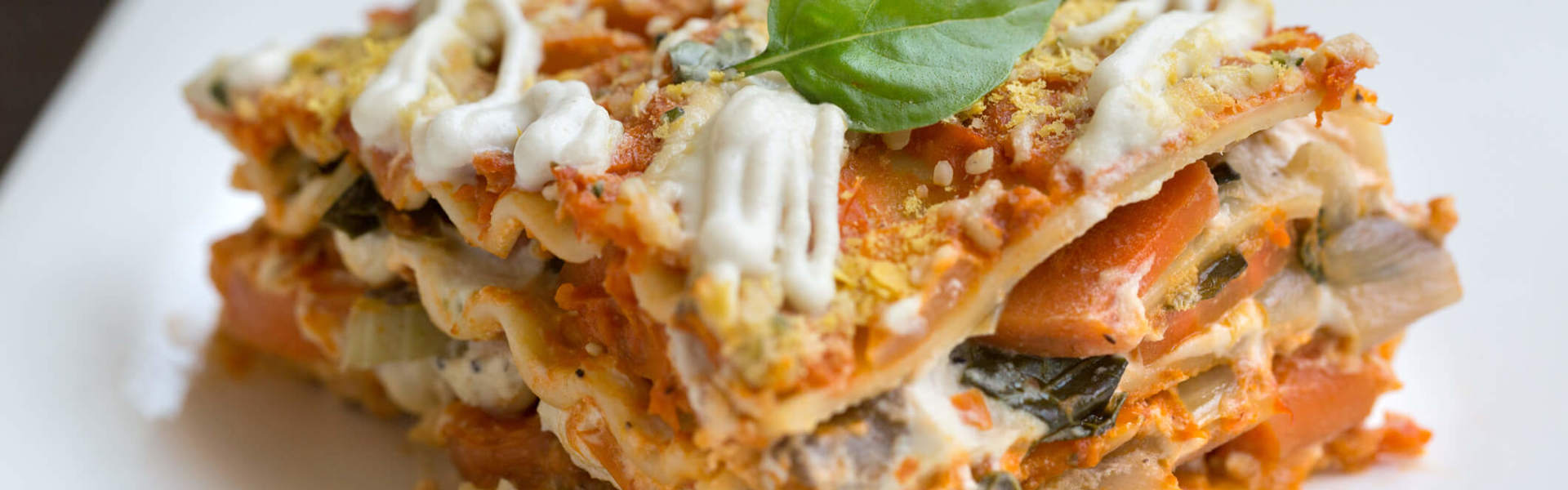 a slice of lentil ricotta spinach lasagne topped with a basil leaf