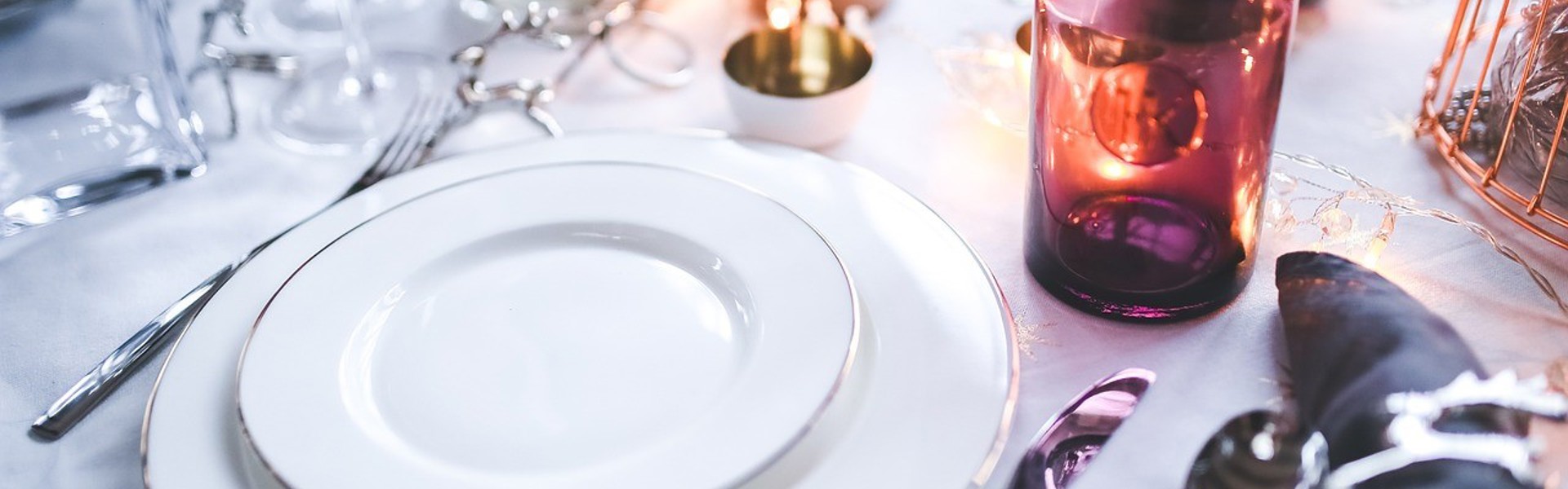 a dinner place setting with white plates and an amber water glass on a white table cloth