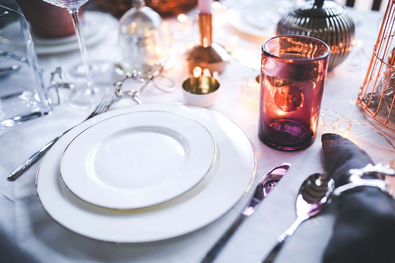 a dinner place setting with white plates and an amber water glass on a white table cloth