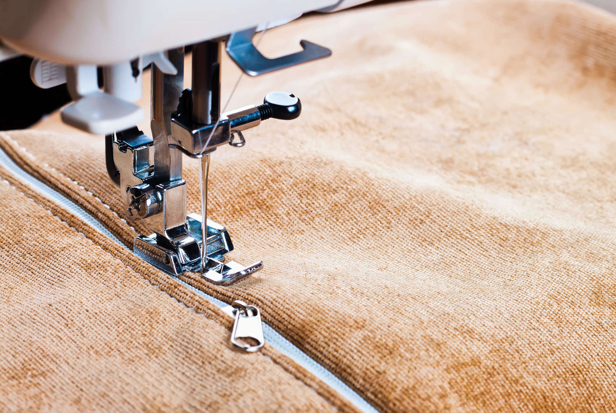A close up of a sewing machine sewing a zip onto a brown velvet jacket