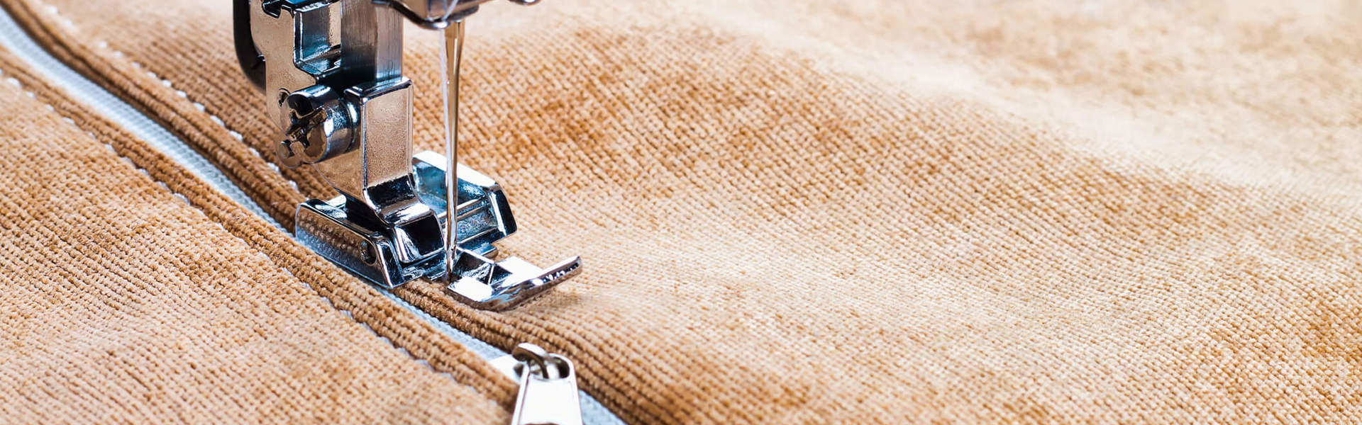 A close up of a sewing machine sewing a zip onto a brown velvet jacket