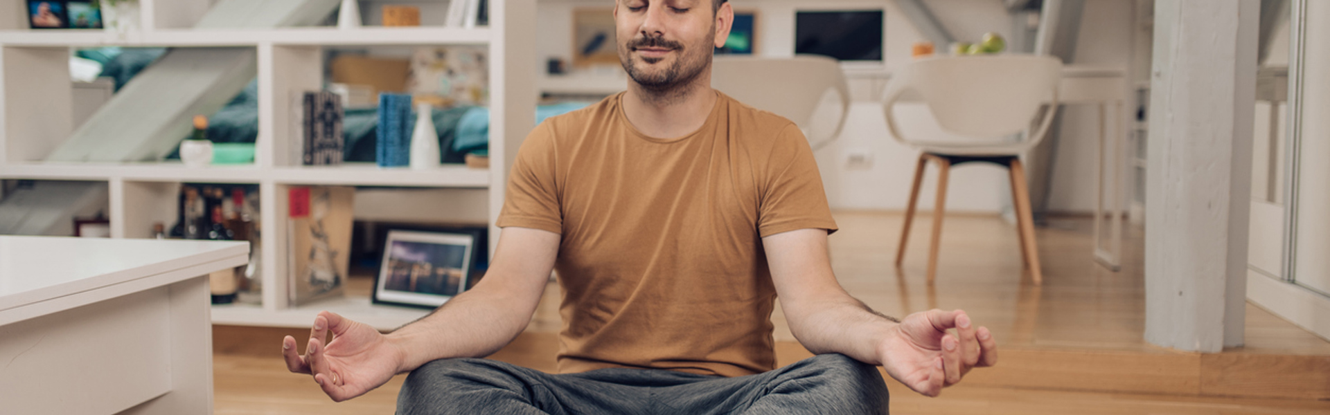 a man sat cross legged on a yoga mat at home doing yoga