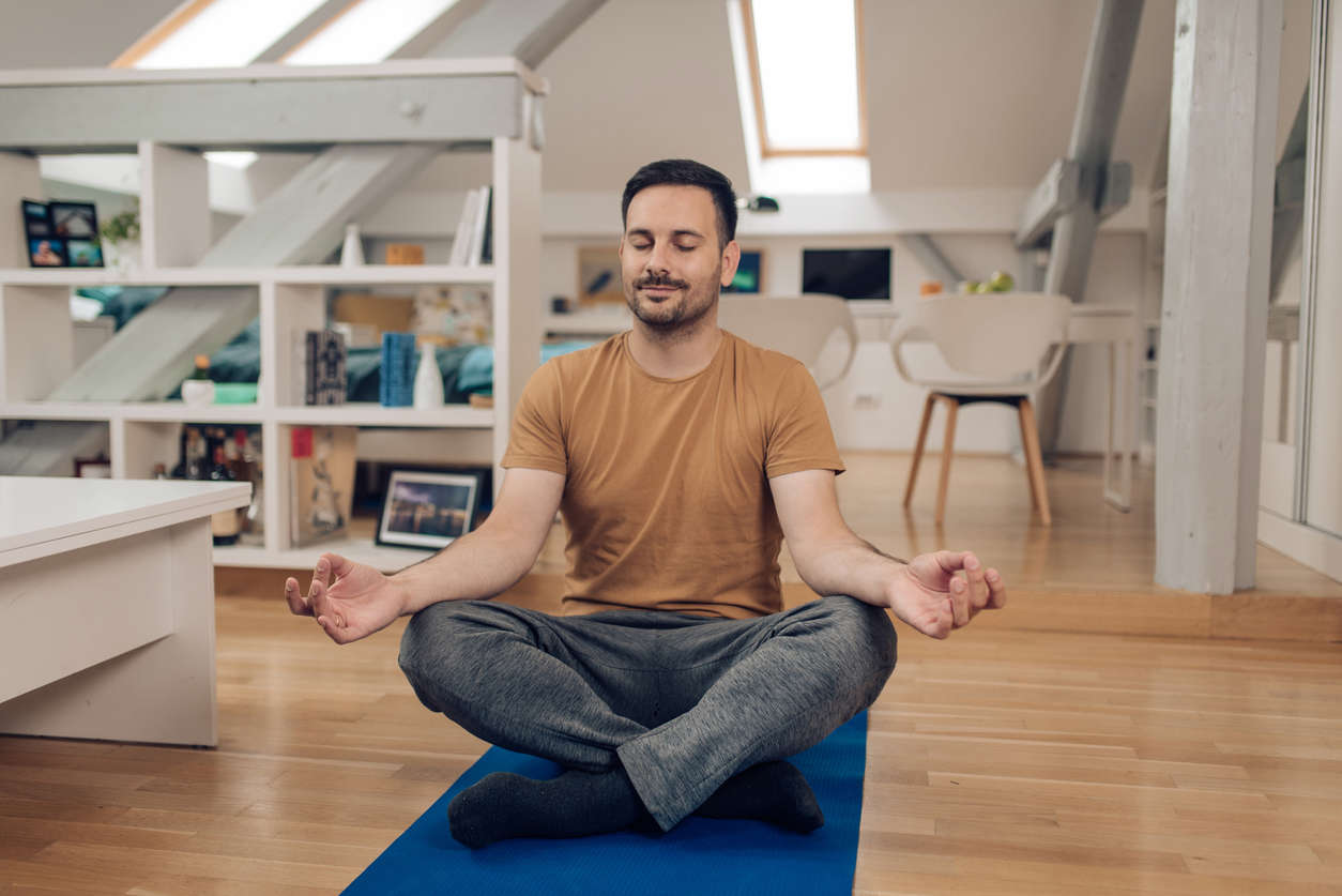 a man sat cross legged on a yoga mat at home doing yoga