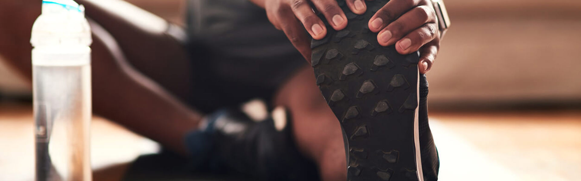 a close up of someone sat on the floor on a workout mat and stretching their hamstrings whilst seated with a water bottle next to their foot