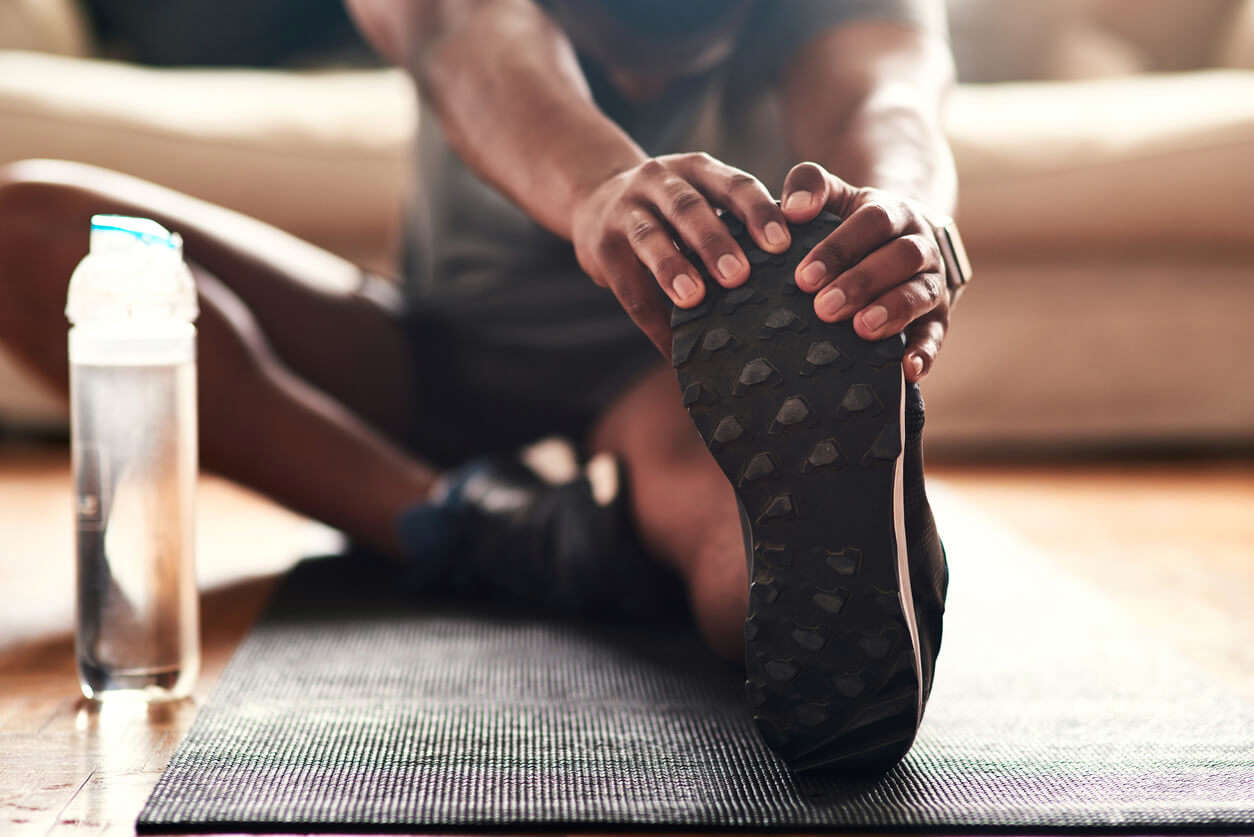 a close up of someone sat on the floor on a workout mat and stretching their hamstrings whilst seated with a water bottle next to their foot