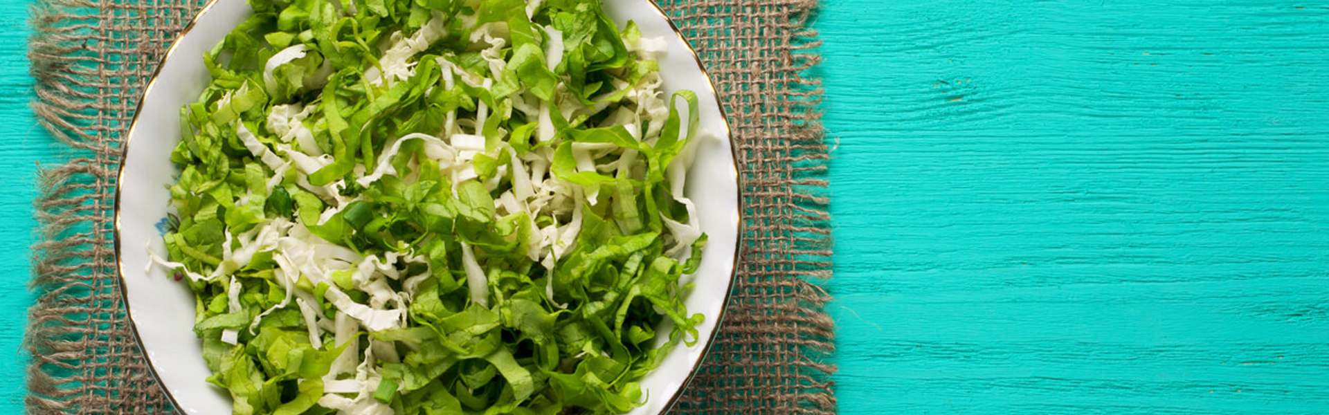 a bowl of cabbage soup resting on a green hessian place mat on a painted turquoise wooden table