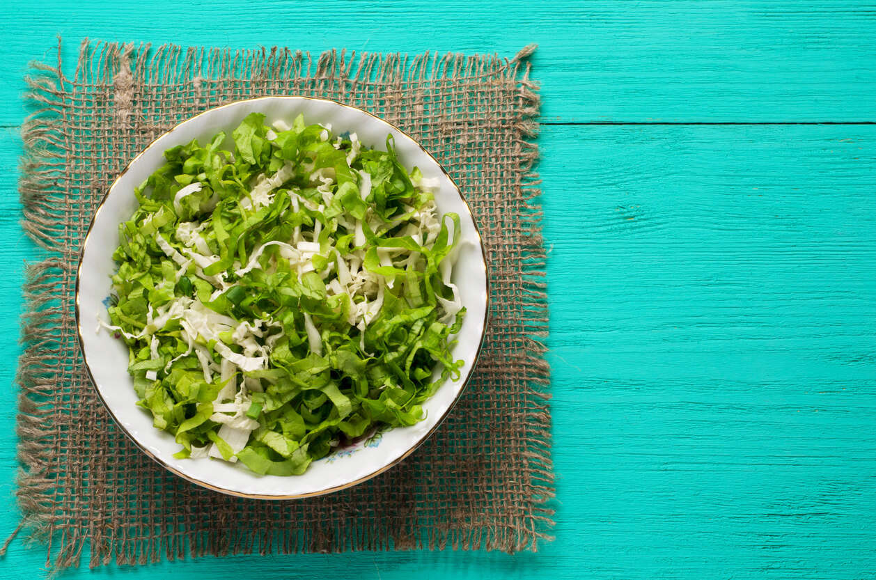 a bowl of cabbage soup resting on a green hessian place mat on a painted turquoise wooden table