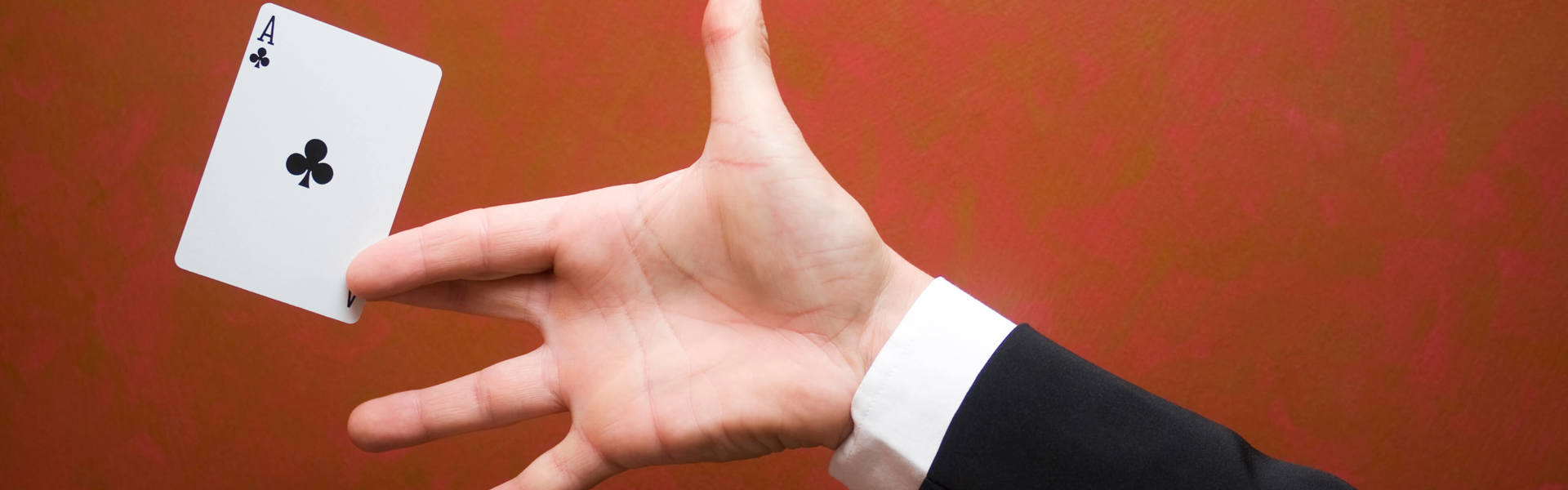 a magician's hand holding a playing card against a red background