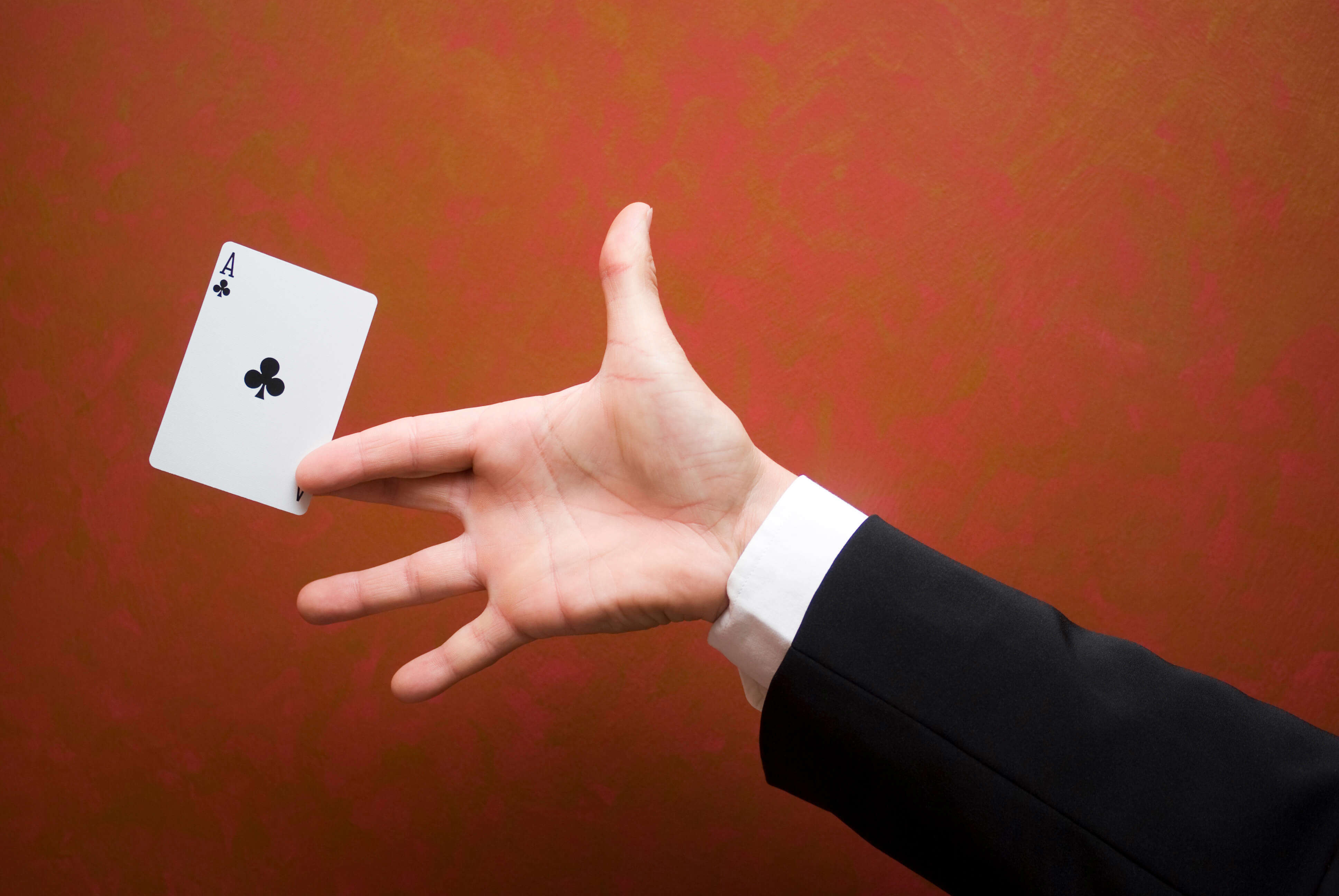 a magician's hand holding a playing card against a red background