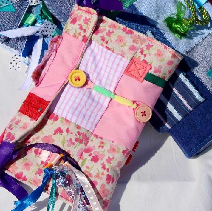Main image: a handmade twiddle muff, a sensory aid/device, made for a person living with dementia or Alzheimer's. Made with scraps of patterned fabric and various tactile items, like buttons, ribbons, zips. 