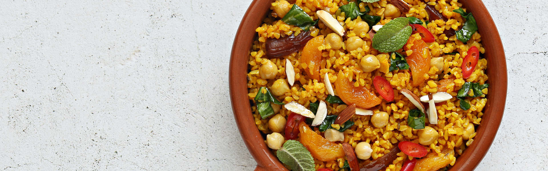 Main image: a bowl of Moroccan Steamed Couscous And Apricot Salad, a healthy vegan recipe, in a brown bowl on a while stone table top.