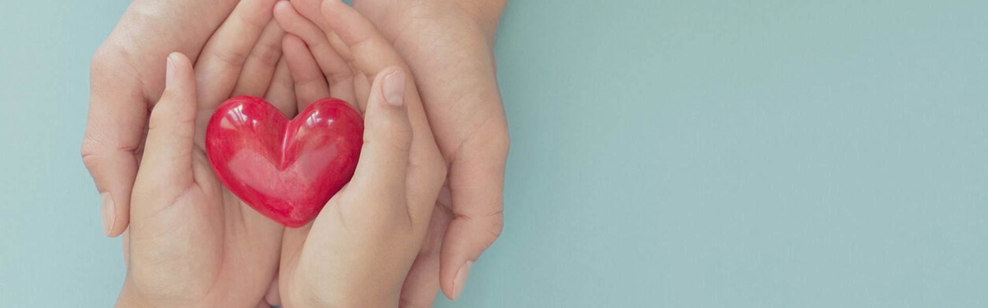 a pair of children's hands holding a red heart, being held by a pair of adult hands on a blue background