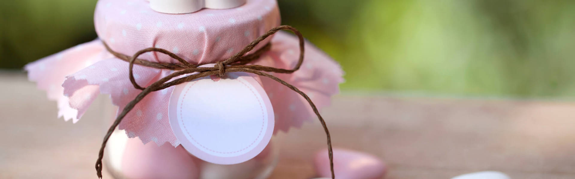 a small wedding favour jar with a pink fabric lid filled with pink and white sweets