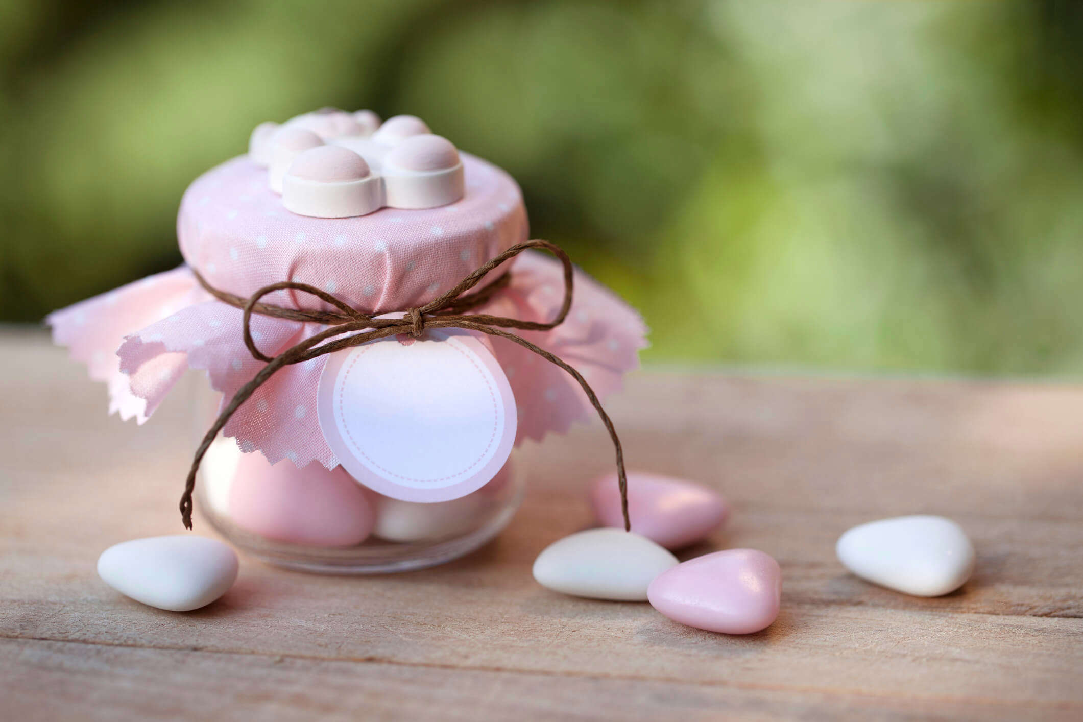 a small wedding favour jar with a pink fabric lid filled with pink and white sweets