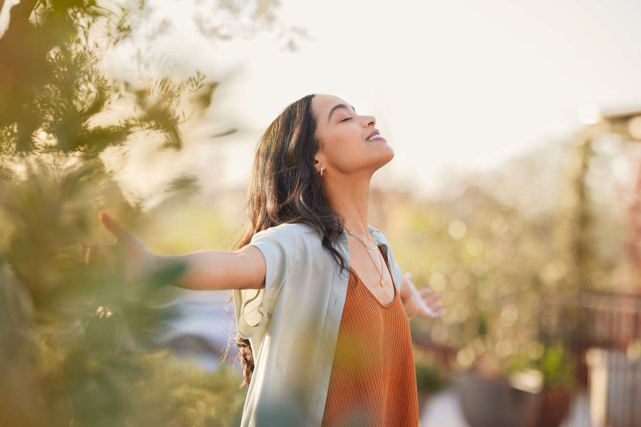 a woman with her arms wide open outside in nature feeling confident