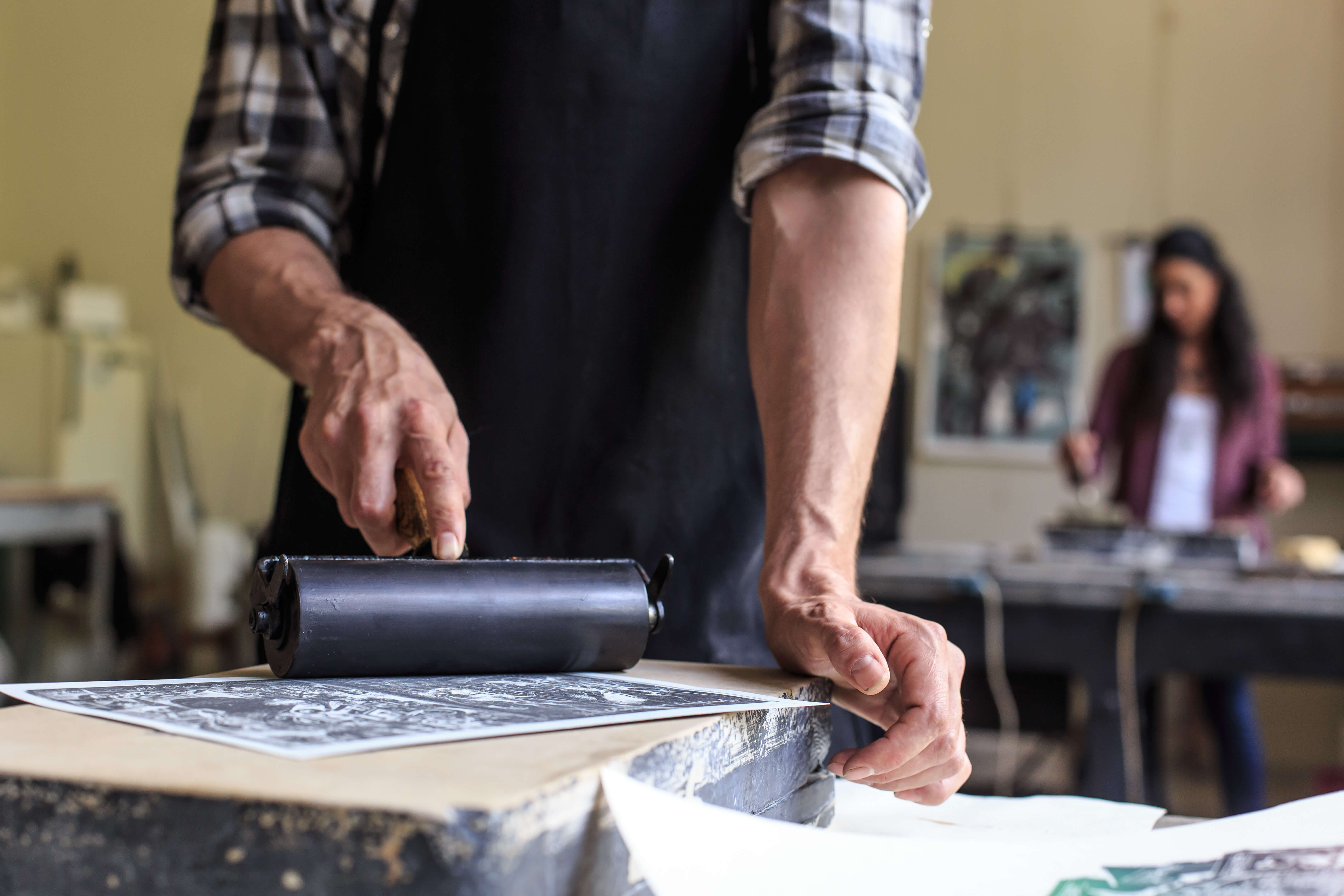 a man wearing an apron using a print roller to create a print work