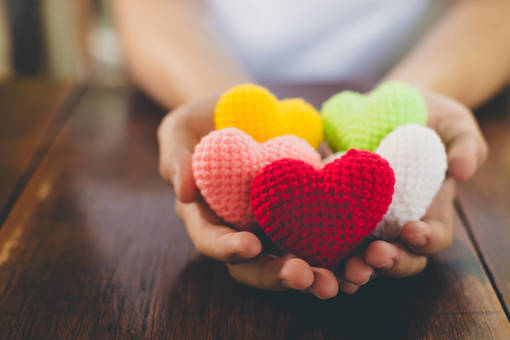 a close up of hands holding multicoloured knitted hearts
