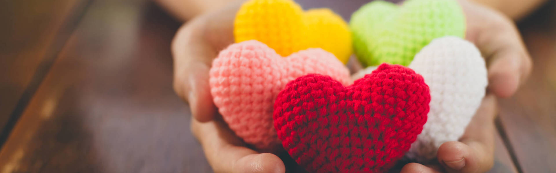 a close up of hands holding multicoloured knitted hearts