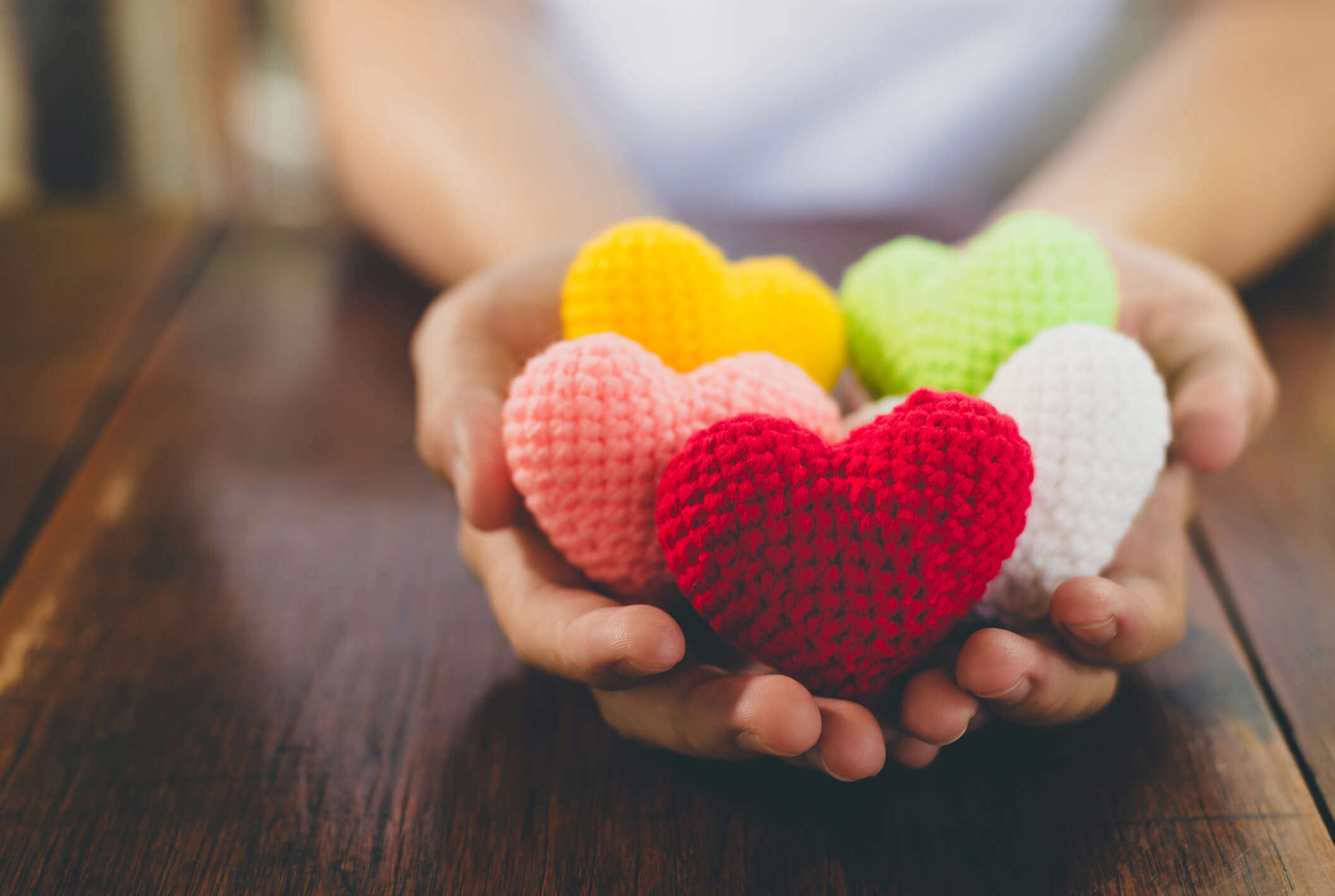 a close up of hands holding multicoloured knitted hearts