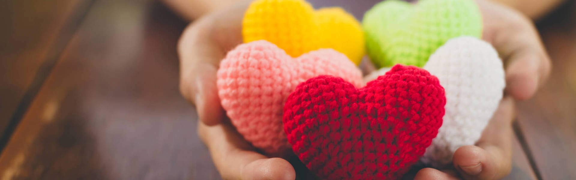 a close up of hands holding multicoloured knitted hearts