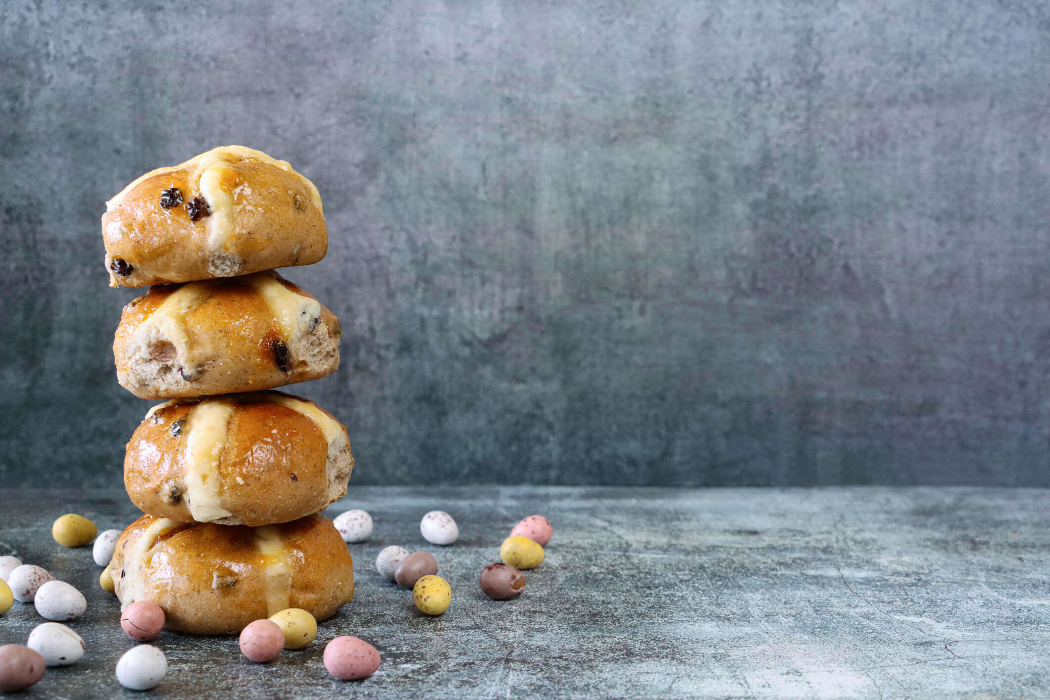 a stack of hot cross buns surrounded by chocolate mini Easter eggs