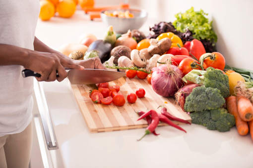 tomatoes being chopped on a wooden chopping board with various vegetables in the background