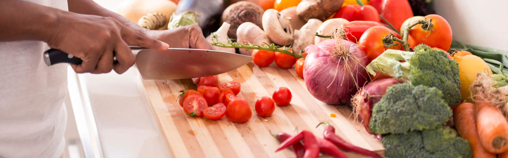 tomatoes being chopped on a wooden chopping board with various vegetables in the background