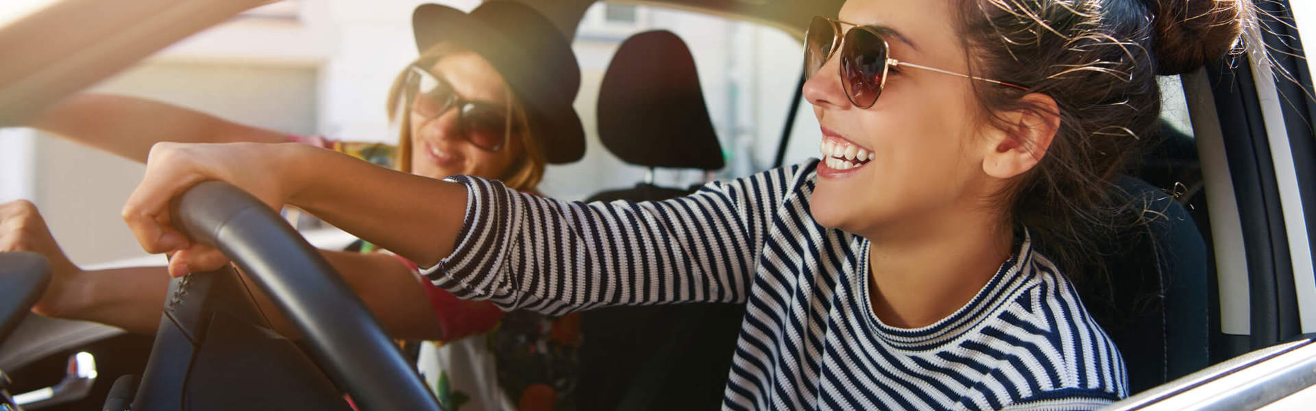 a woman wearing sunglasses driving a car with the window down laughing with a friend