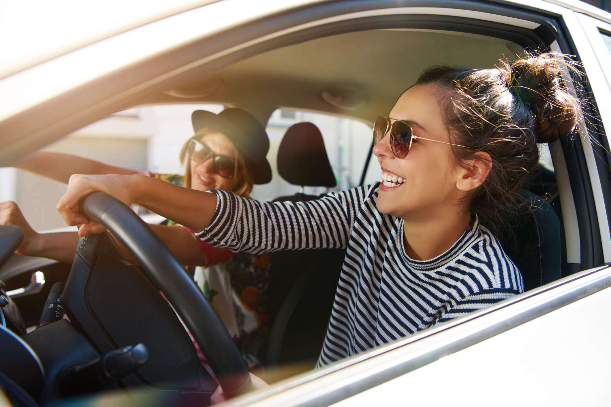 a woman wearing sunglasses driving a car with the window down laughing with a friend