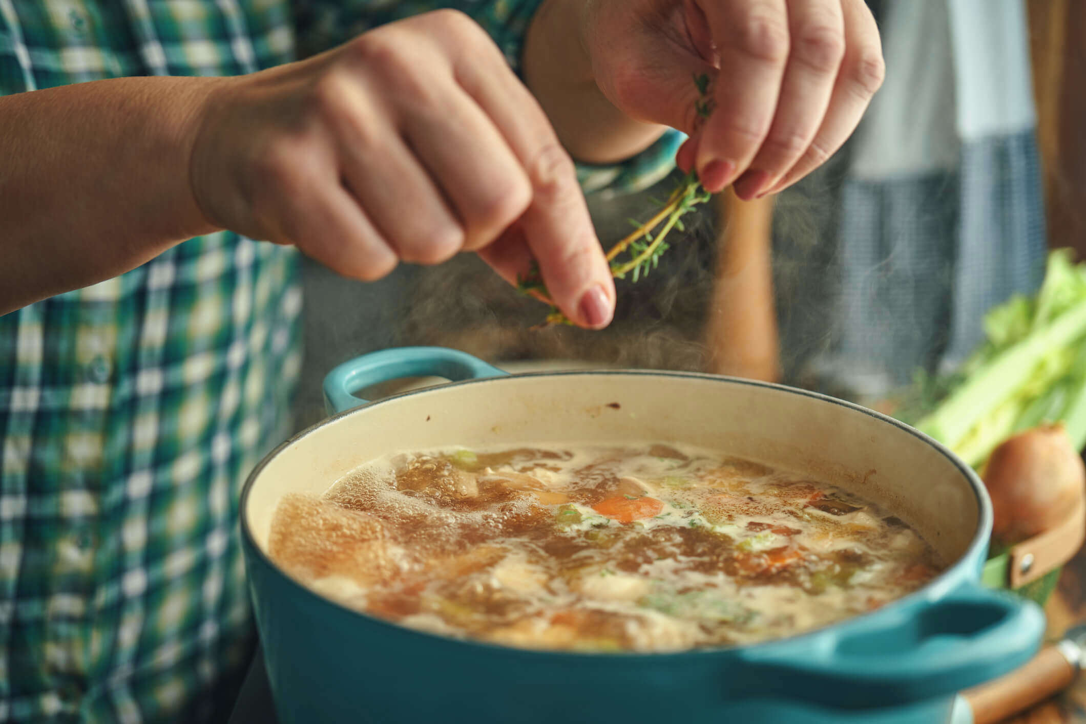 a close up of a cooking chicken and vegetable one pot in a blue cooking pot with someone pinching fresh rosemary into it