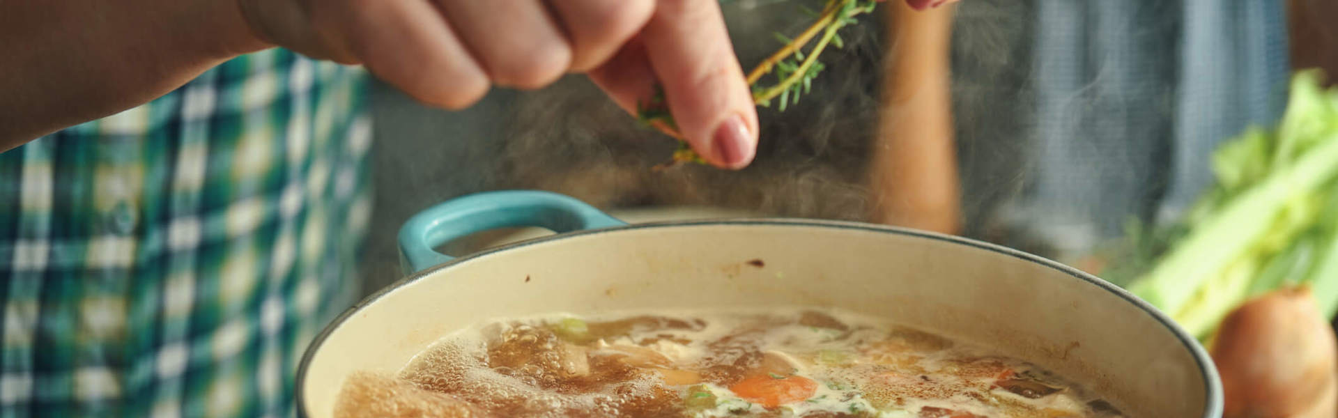 a close up of a cooking chicken and vegetable one pot in a blue cooking pot with someone pinching fresh rosemary into it