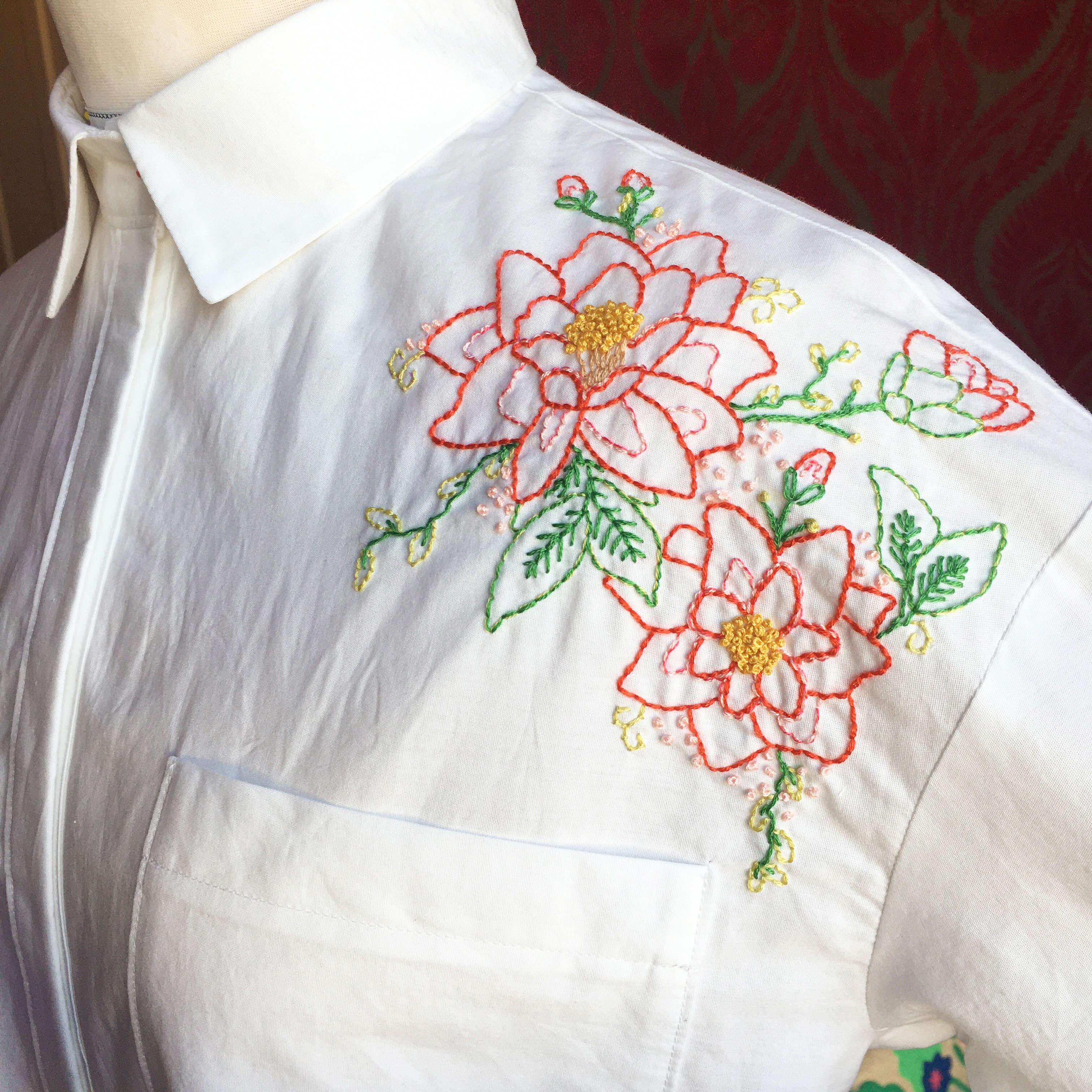 a white shirt with embroidered red and yellow and green flowers made by Serena Baker