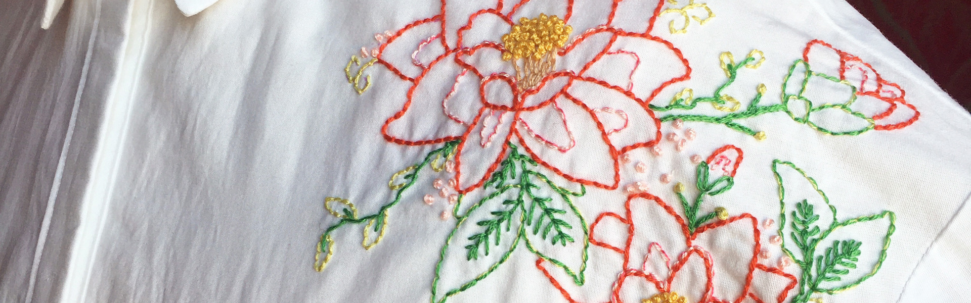 a white shirt with embroidered red and yellow and green flowers made by Serena Baker