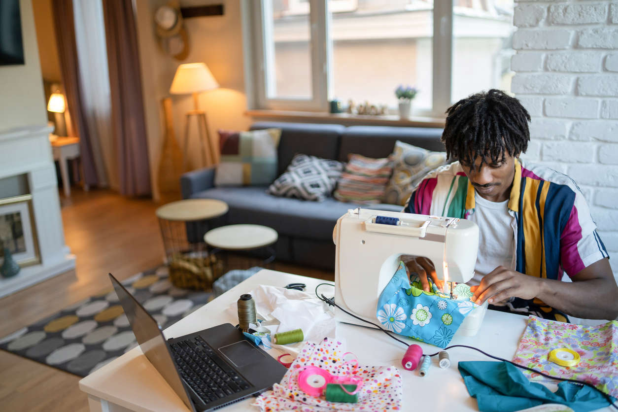 a young man wearing a colourful stripe short sleeved shirt sat at a sewing machine sewing