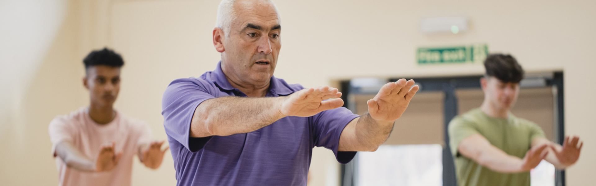 a man wearing a purple polo shirt doing Qi Gong in a group class