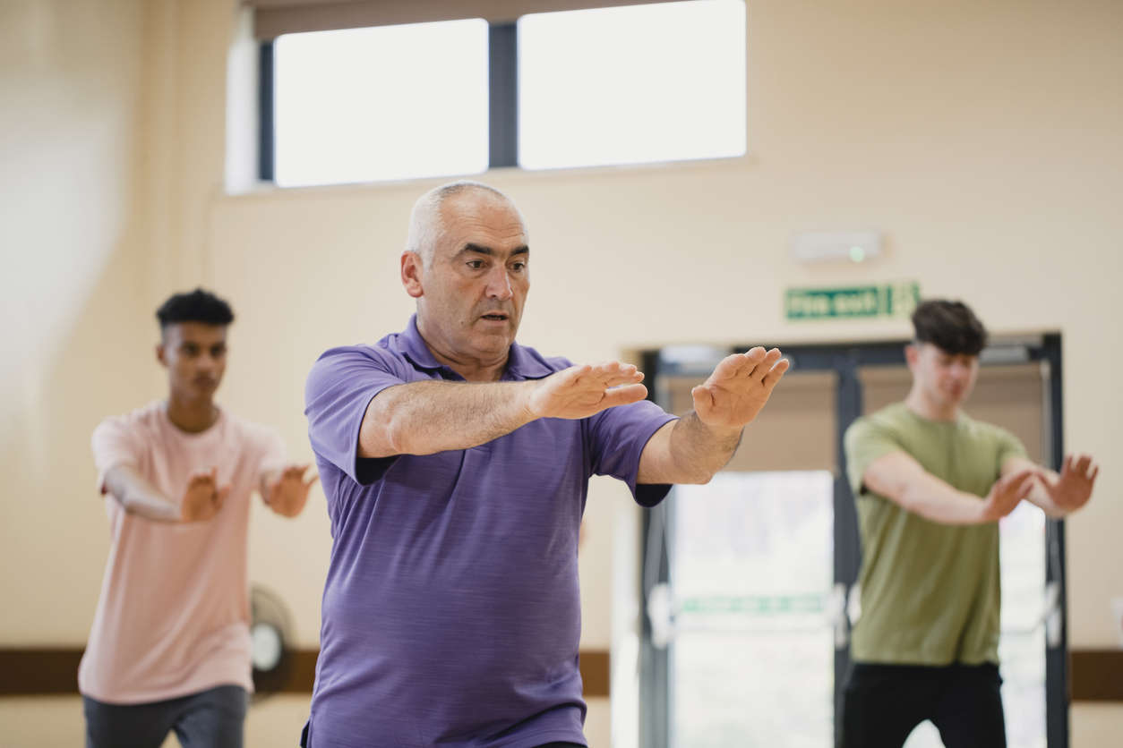 a man wearing a purple polo shirt doing Qi Gong in a group class