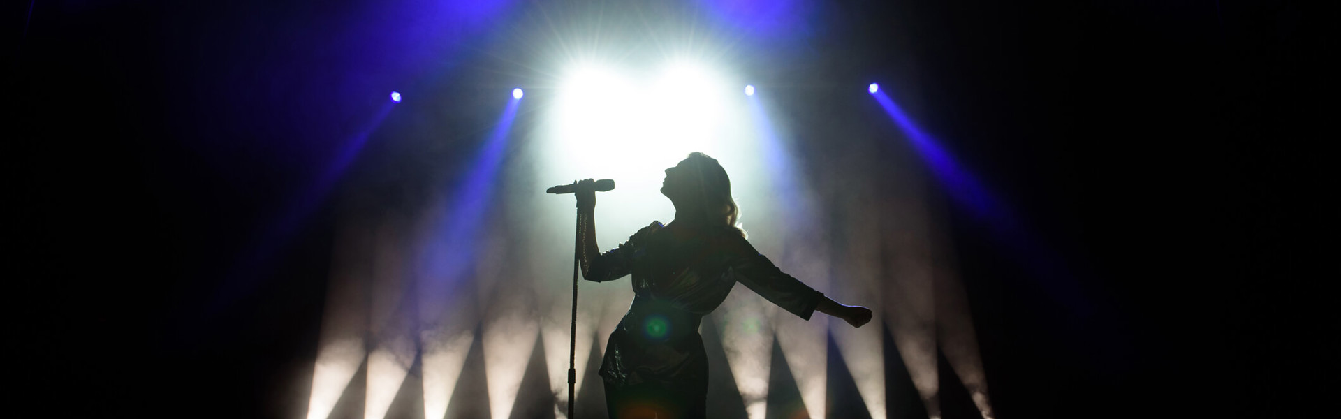 a silhouette of a performer singing into a microphone on stage