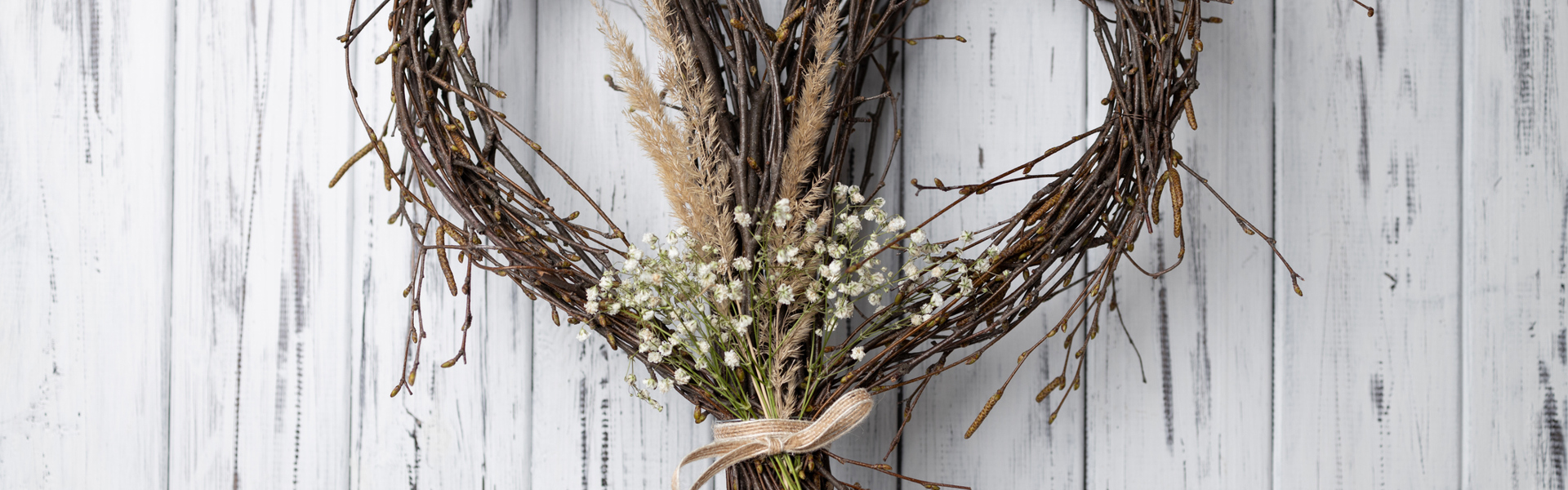 Main Image: A handmade willow heart wreath on a white/grey wooden door.