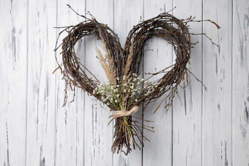 Main Image: A handmade willow heart wreath on a white/grey wooden door.
