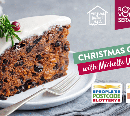 A slice of Christmas cake on a white plate with a small fork next to it and decorating with red berries and rosemary